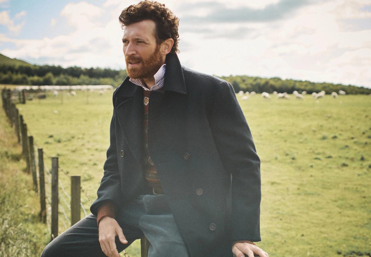 Man in navy Aubin jacket overlooking fields of sheep