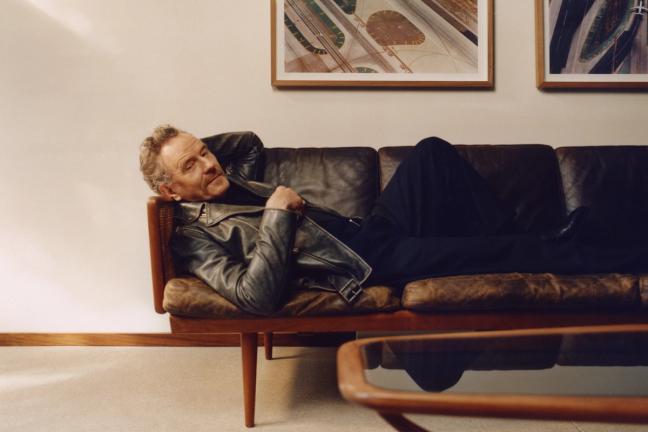 Bryan Cranston reclining on a leather sofa in a Golden Goose jacket