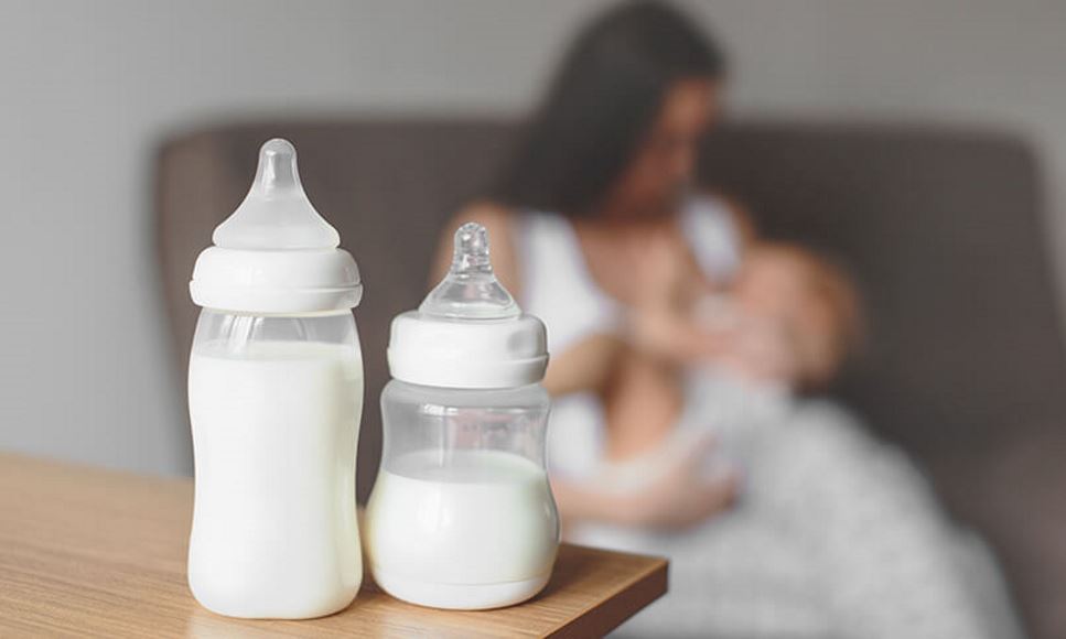 baby bottles in foreground with woman breastfeeding baby in background