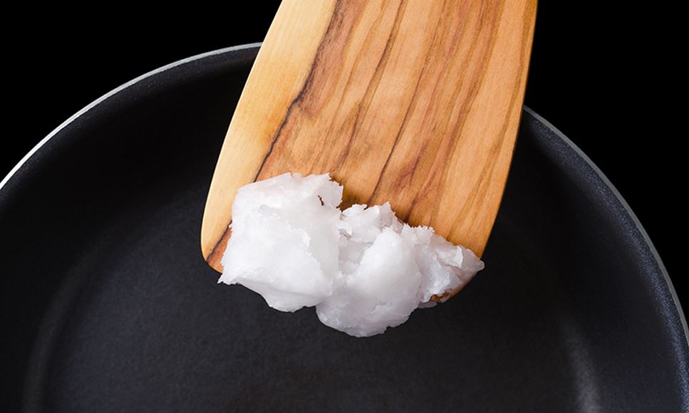 A person is using coconut oil on a spatula and melting it in a pan to cook with it.