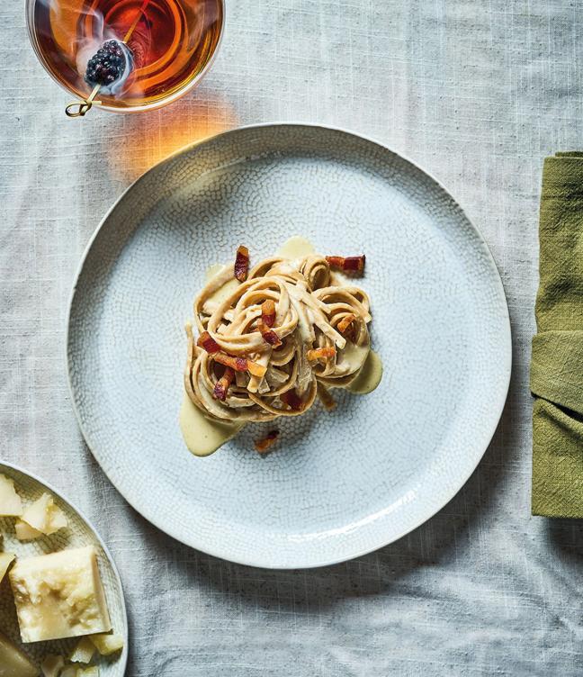 A plate of pasta next to a napkin, cocktail, and some cheese