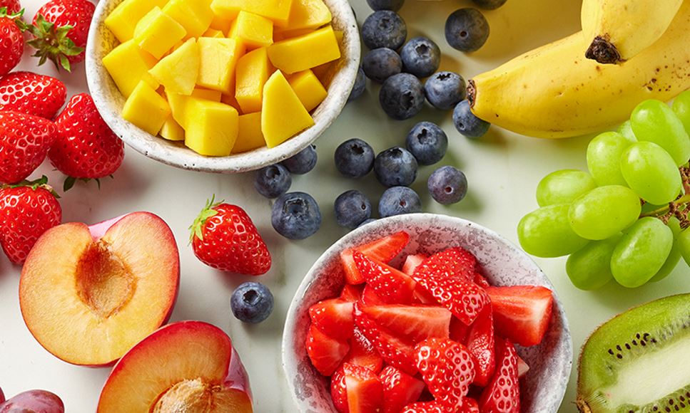 An assortment of fresh fruits including berries, peaches, grapes, mango and bananas.