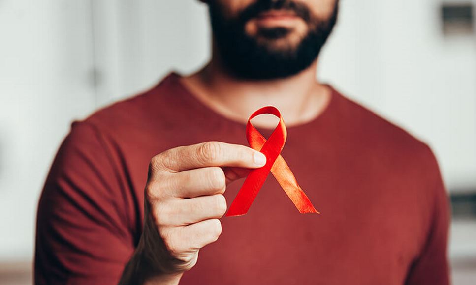 man holding red ribbon representing HIV/AIDS