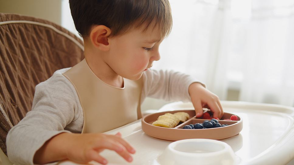 A young boy with PKU (Phenylketonuria) is eating a plate of fresh fruit as part of his PKU-friendly diet.