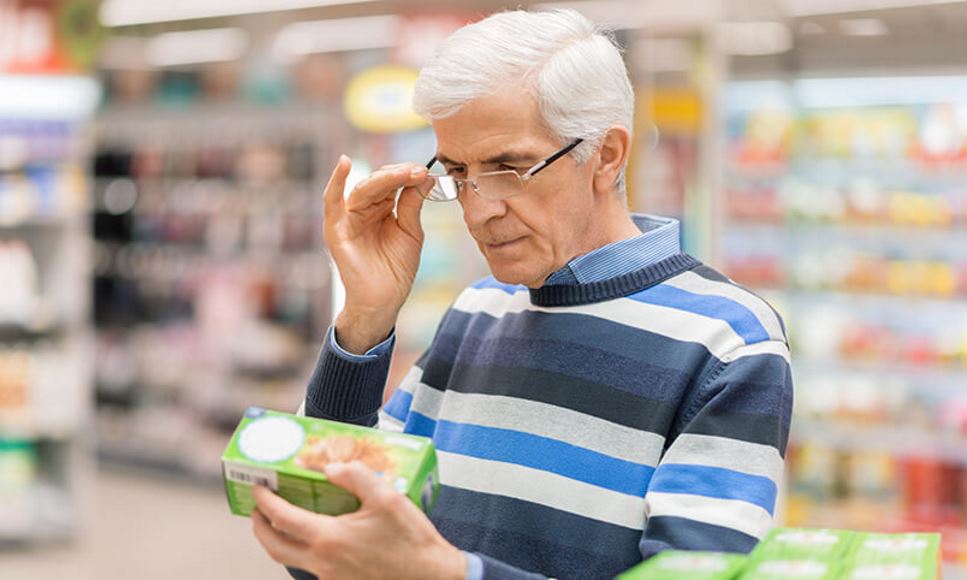 older man reading food label while shopping in grocery store