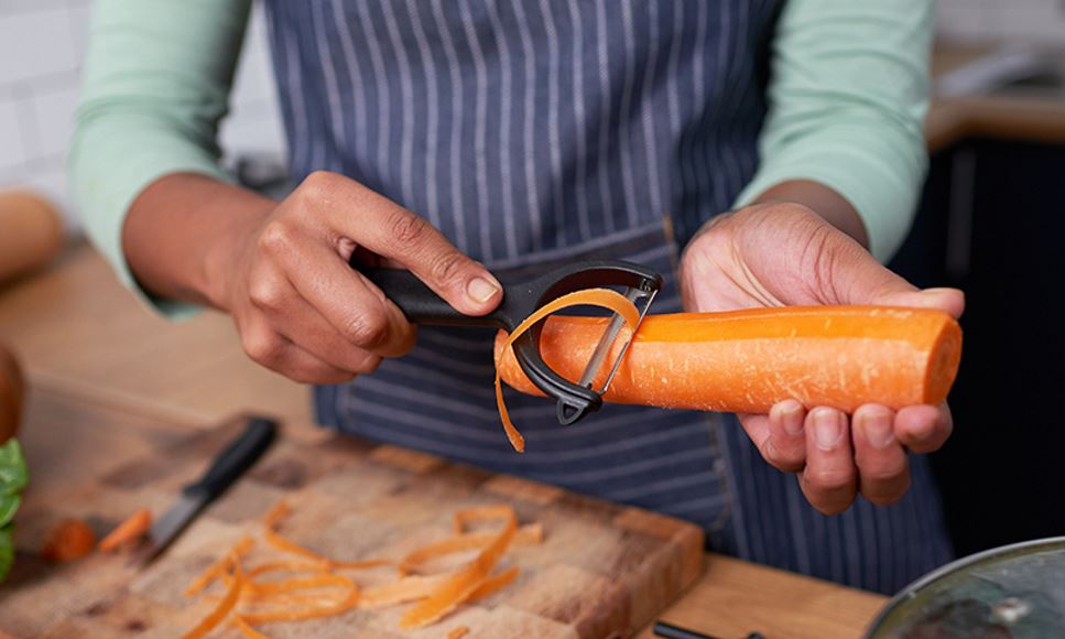 Woman peeling a carrot with a vegetable peeler.