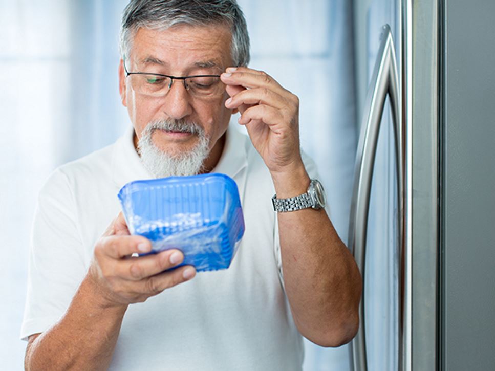 Man looking at food label on mushrooms in his refrigerator to see if they are expired or have a best by/use by date.