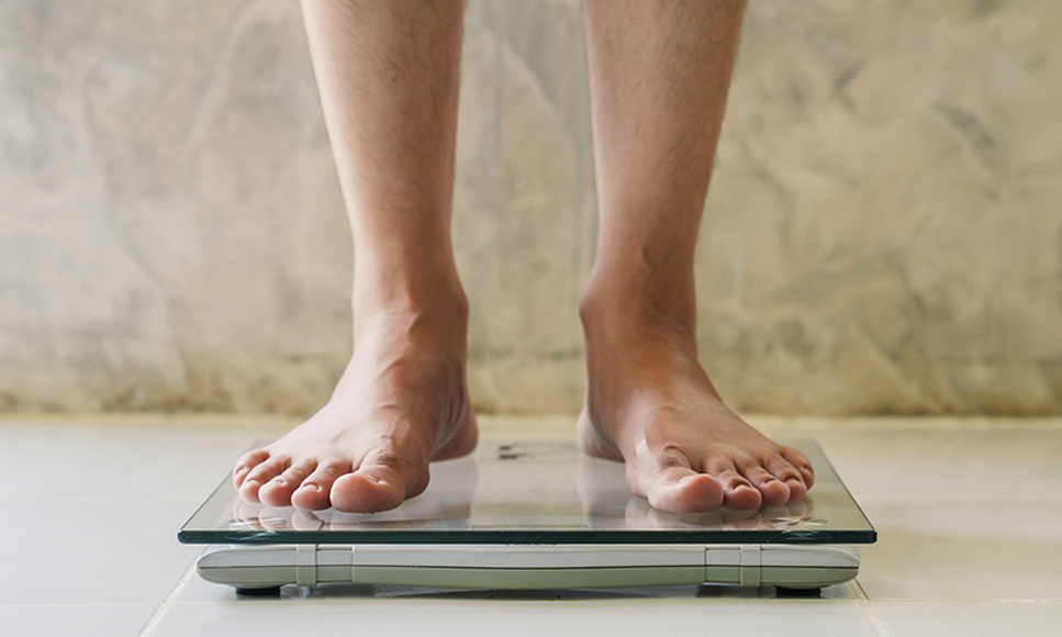 Man with an eating disorder standing on a scale showing that disordered eating can affect men and boys.